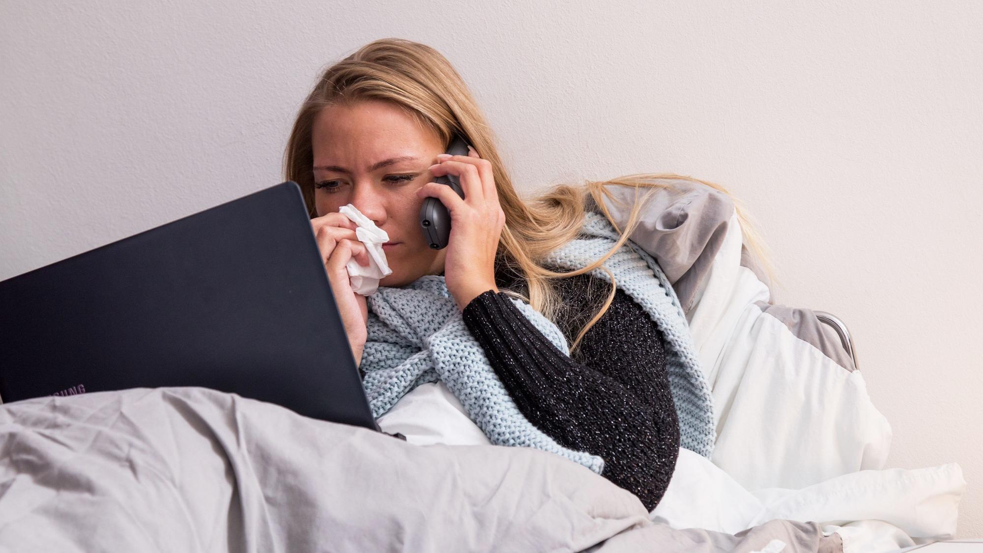 Eine Frau führt aus dem Bett in Telefonat am Handy.