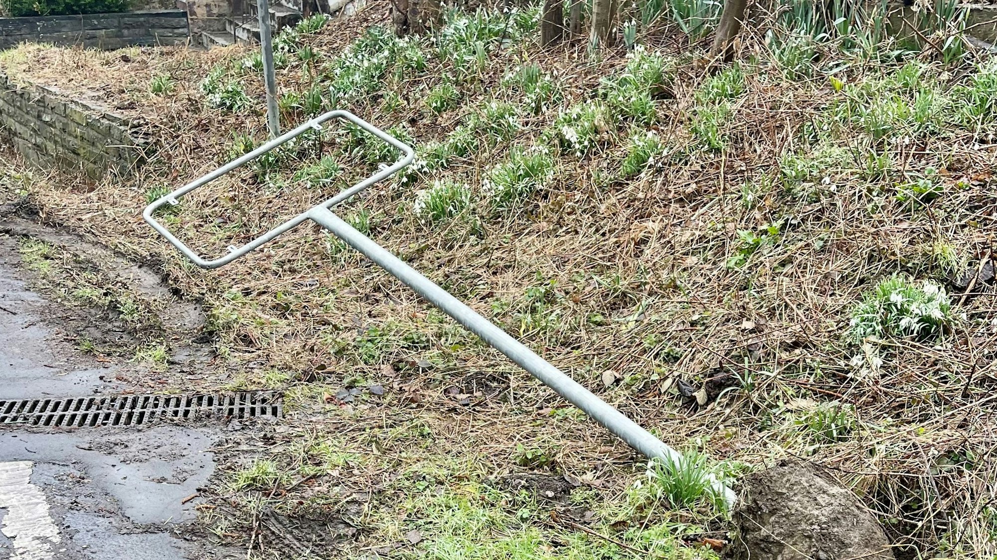 Der Rahmen eines Ortsschildes liegt auf der Wiese im Schlamm.