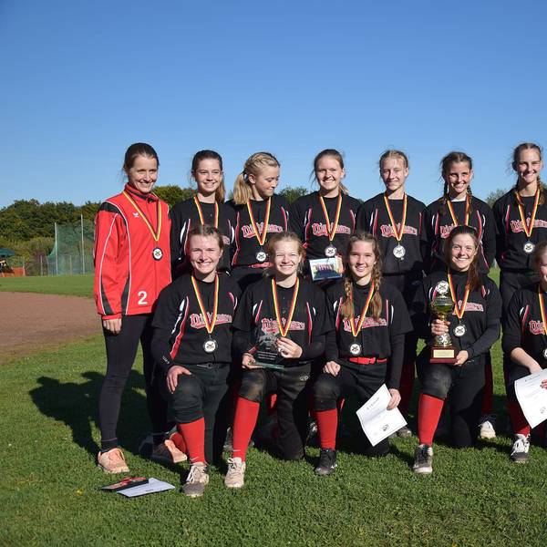 Die Softballerinnen posieren mit umgehangenen Medaillen, Urkunden und dem Pokal für ein Foto.