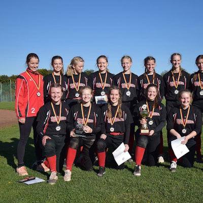 Die Softballerinnen posieren mit umgehangenen Medaillen, Urkunden und dem Pokal für ein Foto.