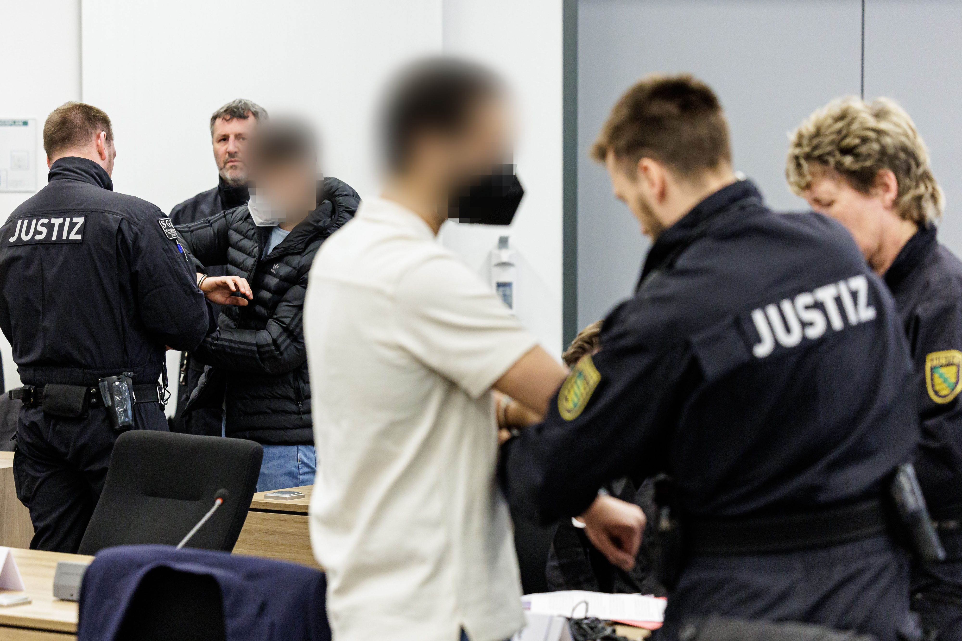 Die Angeklagten Mohamed R. (3.v.r.) und Bashir R. (3.v.l.) werden von Justizbeamten in Handschellen in den Gerichtssaal des Oberlandesgerichts Dresden geführt.