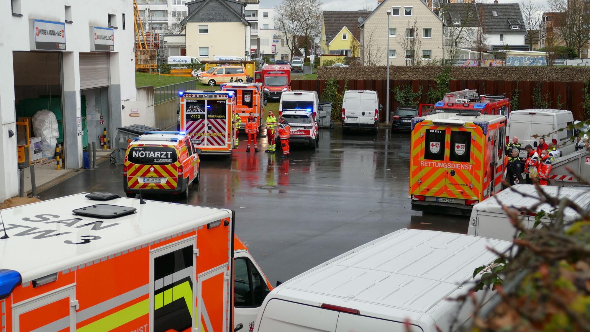 Auf einem regennassen Hinterhof stehen Fahrzeuge von Rettungsdienst und Notarzt, Einsatzkräftee stehen daneben.