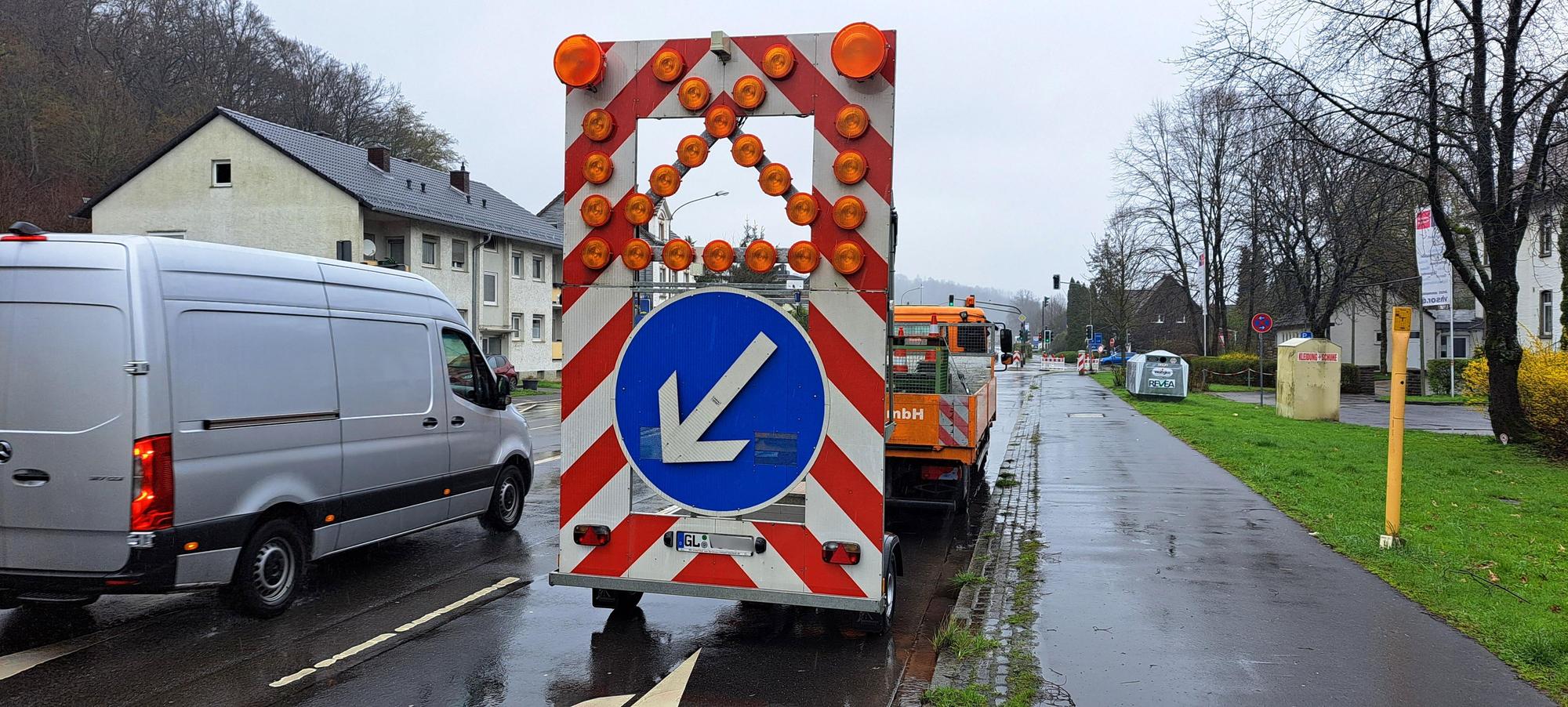 Eine Verkehrstafel, die auf einem Anhänger hinter einem Lkw montiert ist, zeigt an, dass Autofahrer nach links ausweichen müssen und die weitere Spur, auf der das Gespann steht, gesperrt ist.