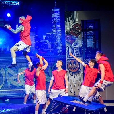 Das Bild zeigt sechs junge Männer, die akrobatisch von einem Trampolin an einen Basketballkorb springen.