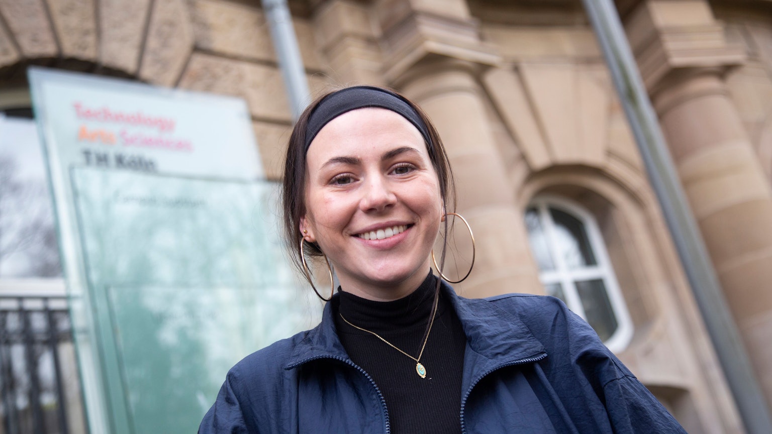 Die Studentin Viviana Picerno steht lächelnd vor dem Eingang der Technischen Hochschule Köln.
