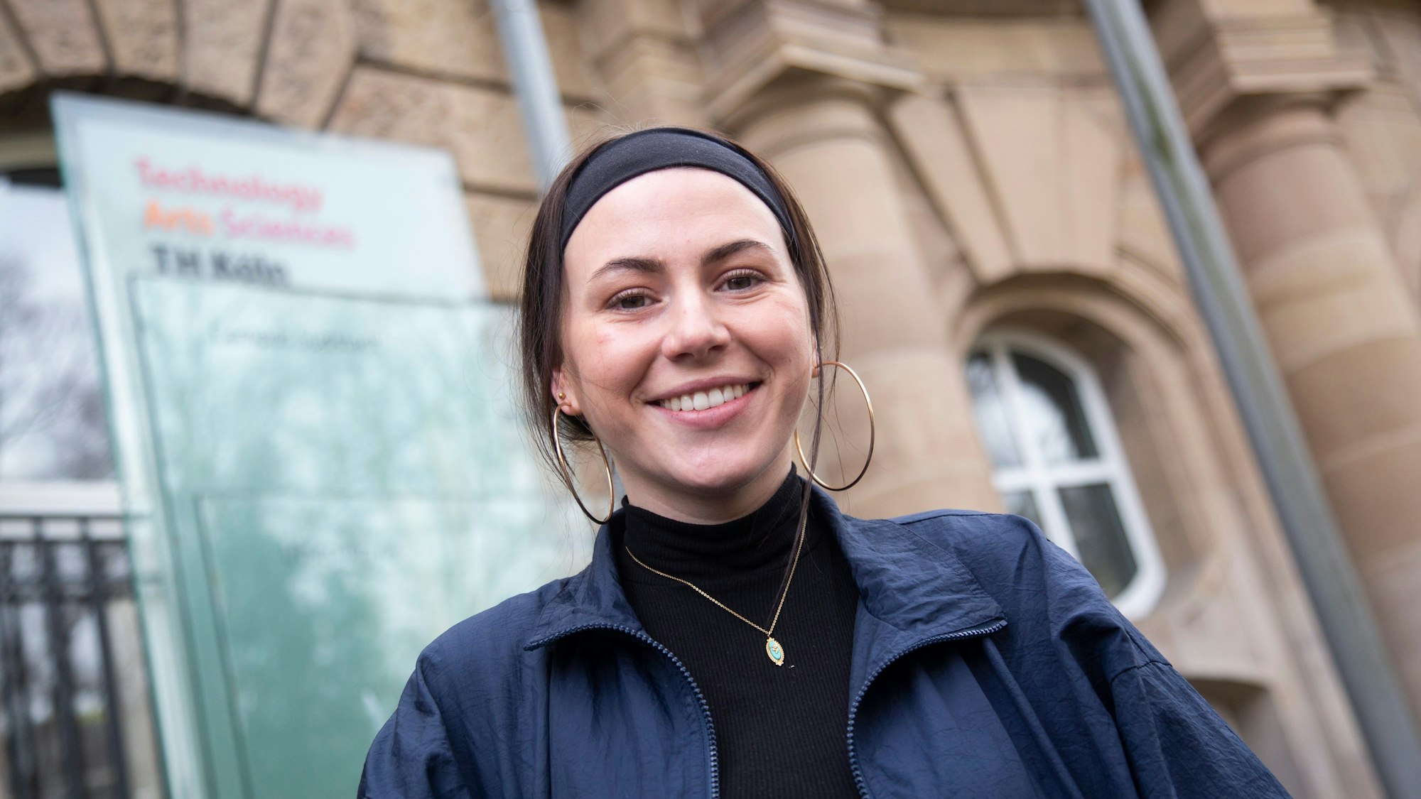Die Studentin Viviana Picerno steht lächelnd vor dem Eingang der Technischen Hochschule Köln.
