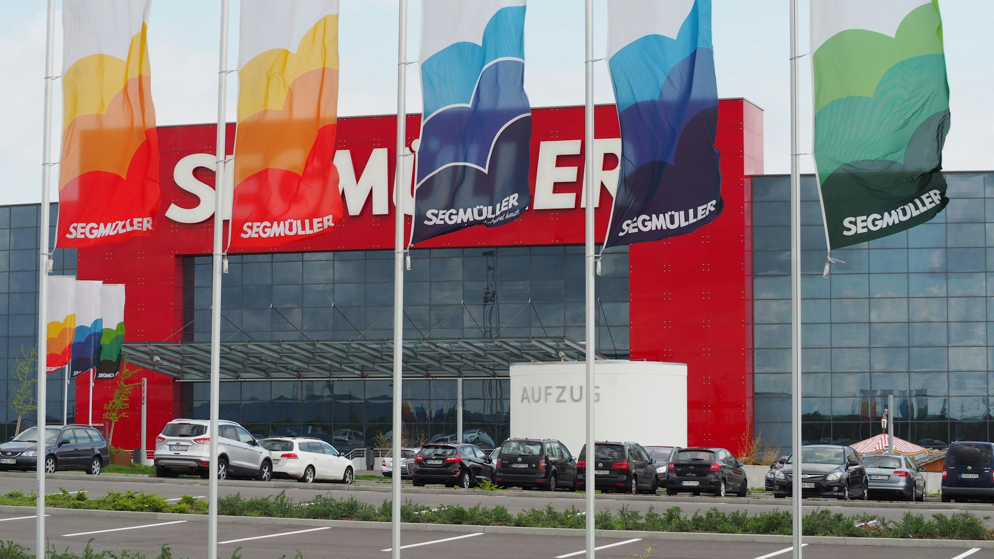 Auf dem Foto sind parkende Fahrzeuge und die Fassade des Einrichtungshauses zu sehen.