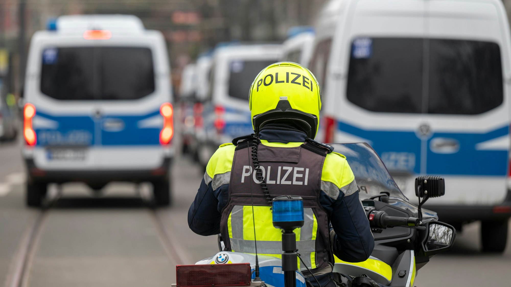 Ein Polizist fährt auf einem Motorrad hinter unscharfen Einsatzfahrzeugen. (Symbolbild)