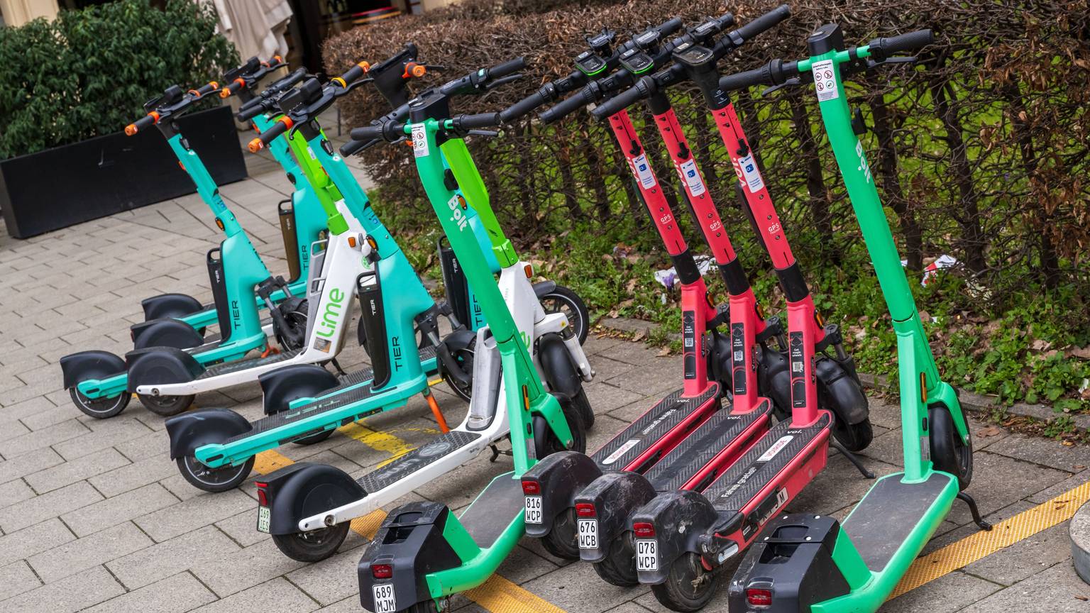 E-Scooter von verschiedenen Anbietern stehen in der Innenstadt auf einem markierten Abstellplatz.