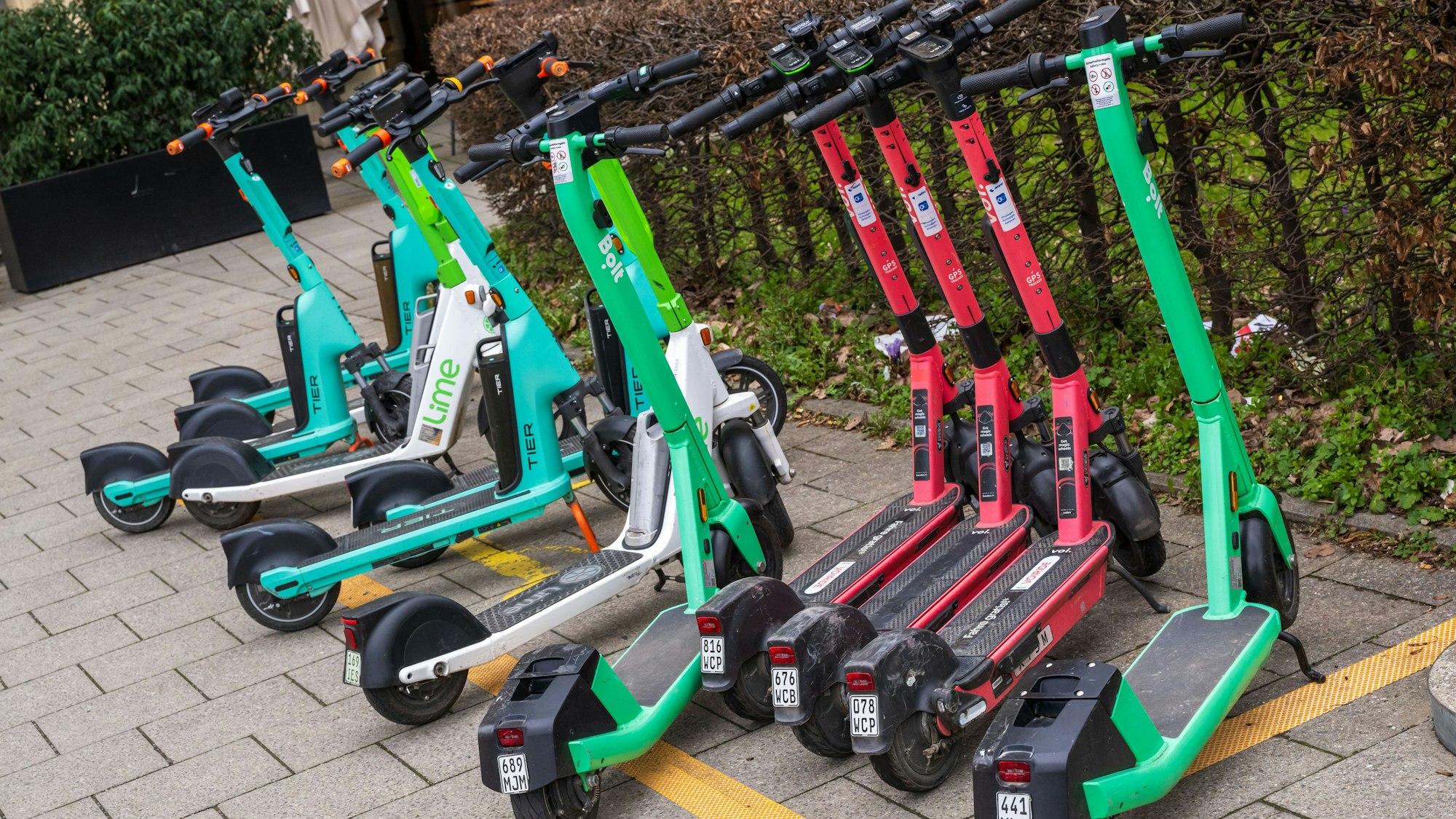 E-Scooter von verschiedenen Anbietern stehen in der Innenstadt auf einem markierten Abstellplatz.