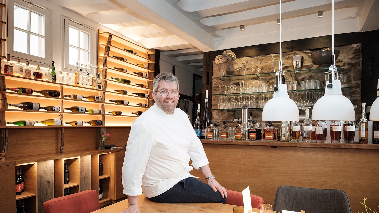 Lokal „Anna Seibert“ in Rheinbach von Benedikt Frechen. Der Inhaber sitzt auf einem Tisch in seinem Lokal.