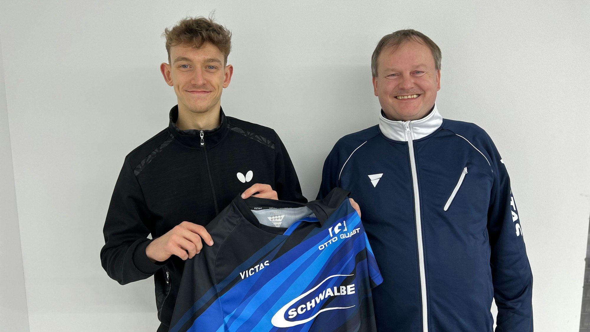 Zwei Männer stehen nebeneinander. Der Jüngere hält sein neues Trikot des Tischtennis-Bundesligisten aus Bergneustadt in den Händen.