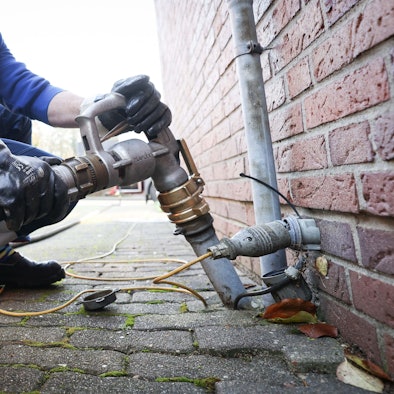 Ein Mitarbeiter eines Diesel- und Heizöl-Unternehmens befestigt die Zapfpistole an einem Füllstutzen für die Heizöllieferung an einen Kunden in einem Einfamilienhaus.