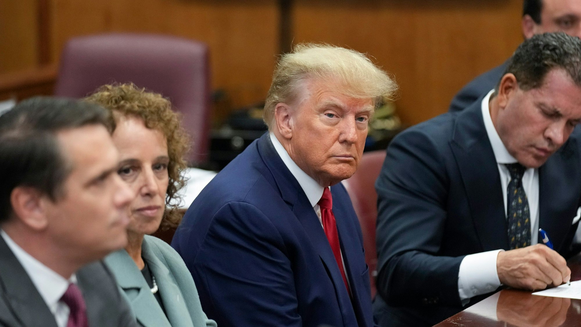 Donald Trump (M), ehemaliger Präsident der USA, sitzt in einem Gerichtssaal in Manhattan mit seinem Verteidigungsteam am Tisch.
