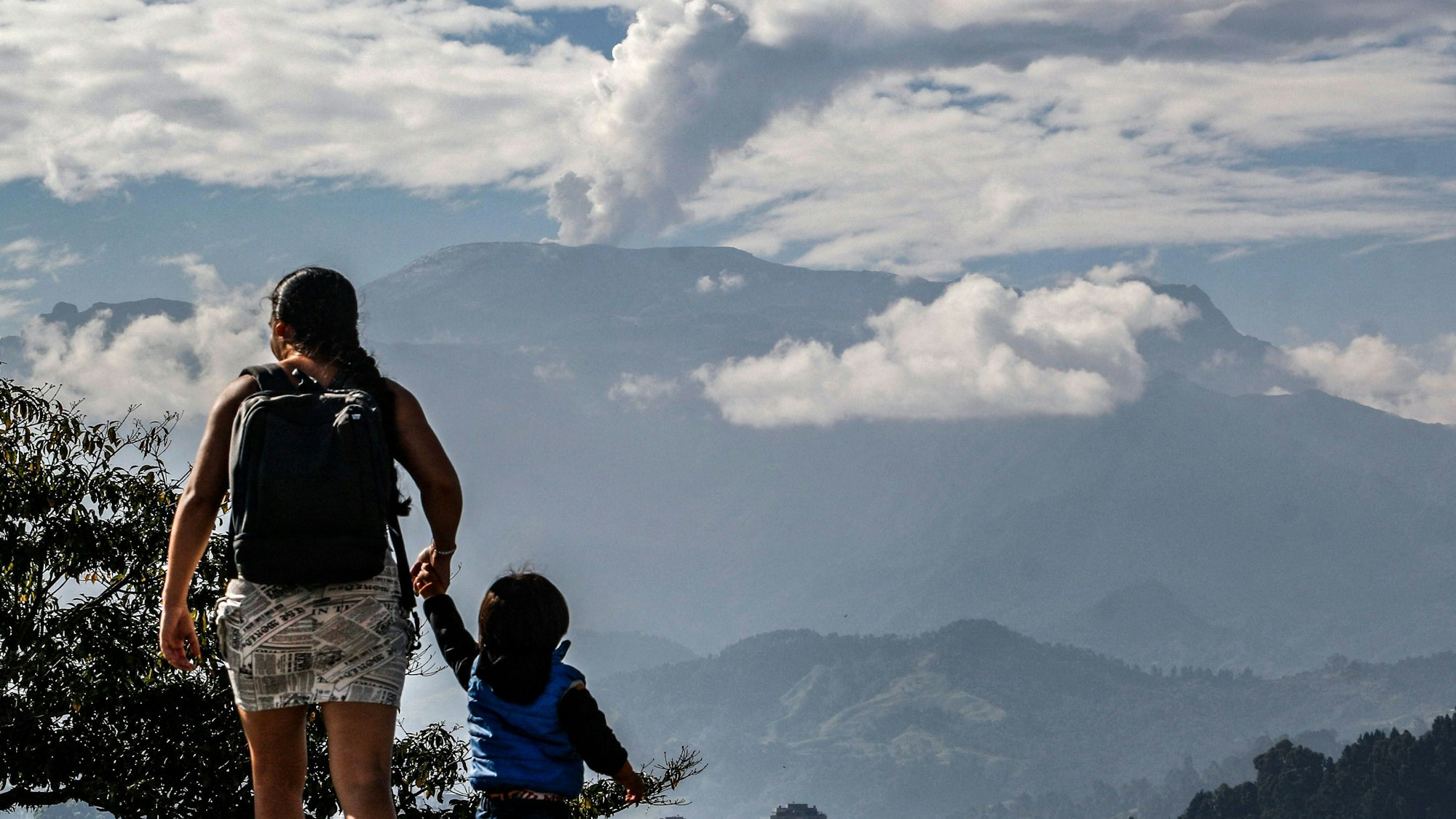 Es ist eine Mutter mit ihrem Kind an der Hand zu sehen. Im Hintrgrund steht der Vulkan.