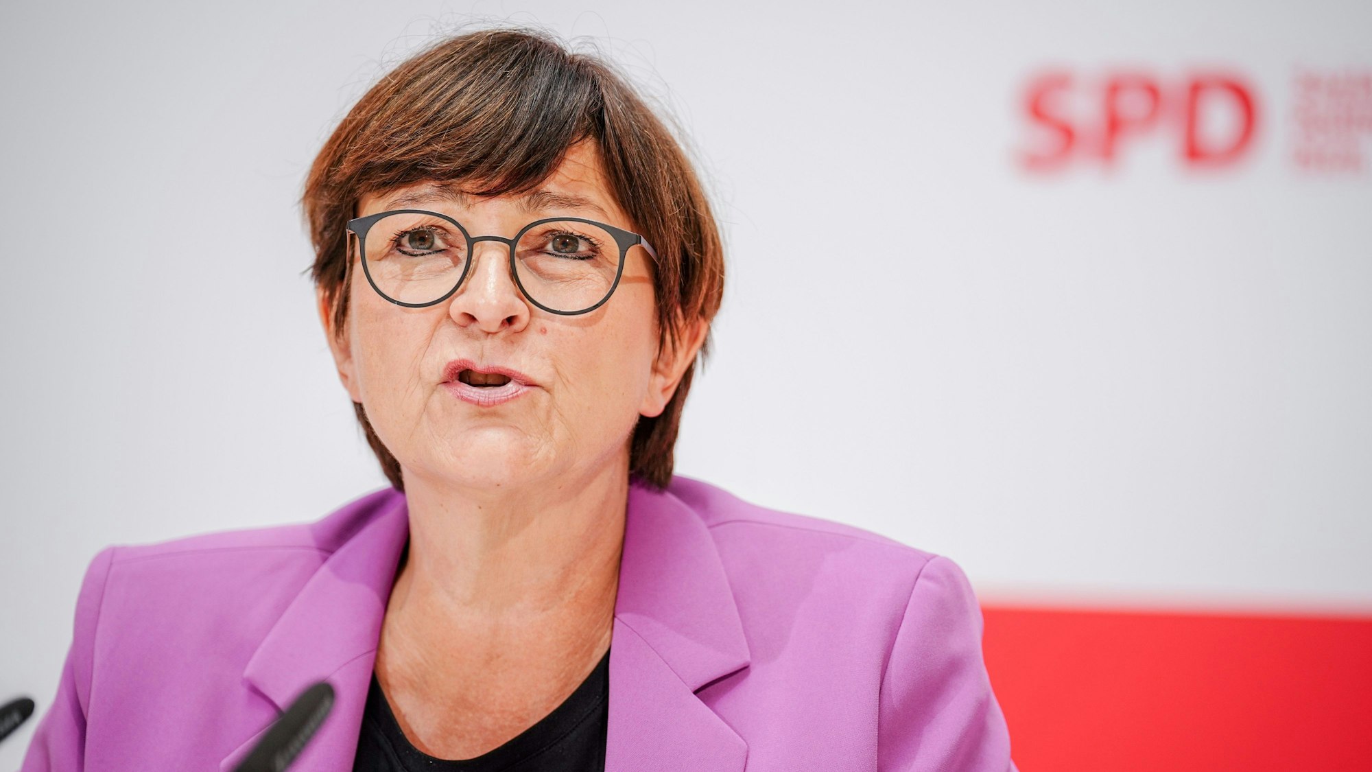 Saskia Esken, SPD-Bundesvorsitzende, spricht auf einer Pressekonferenz vor einer unscharfen weiß-roten Wand mit SPD-Logo.