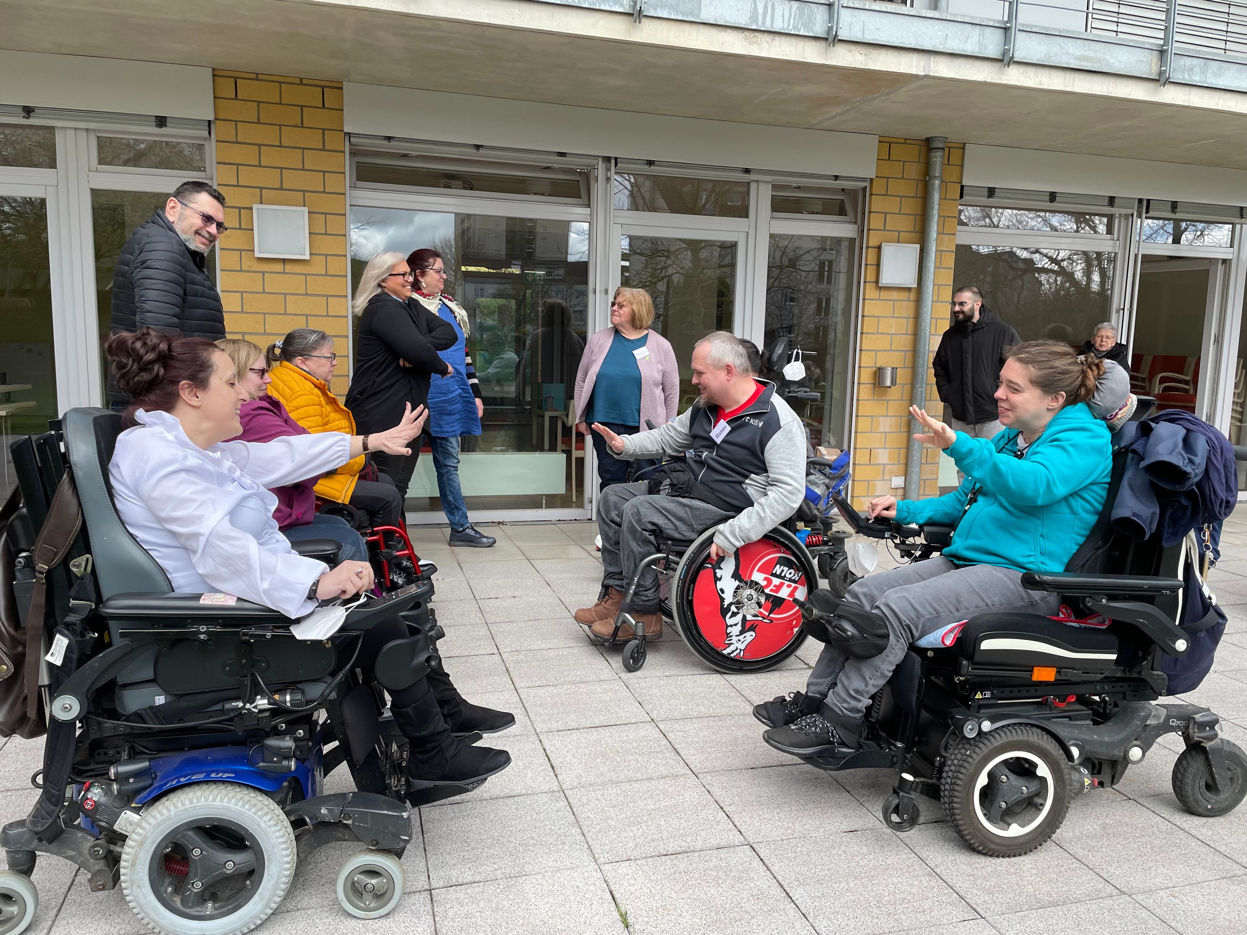 Männer und Frauen in Rollstühlen sitzen sich gegenüber und lächeln.