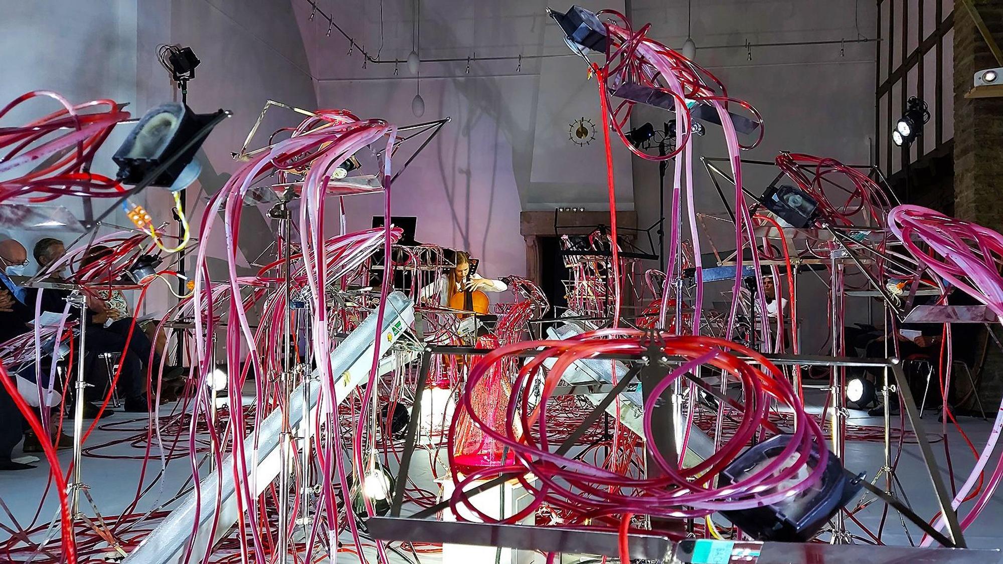 Knäuel aus, mit roter Flüssigkeit gefüllten, Schläuchen umgeben die Cellistin Valerie Fritz bei der Konzert-Kunstinstallation „Nuqta – The beginning“ im Galeriesaal des Hauses für Lehrerfortbildung, dem Herzstück des dreitägigen Festivals in Kronenburg.
