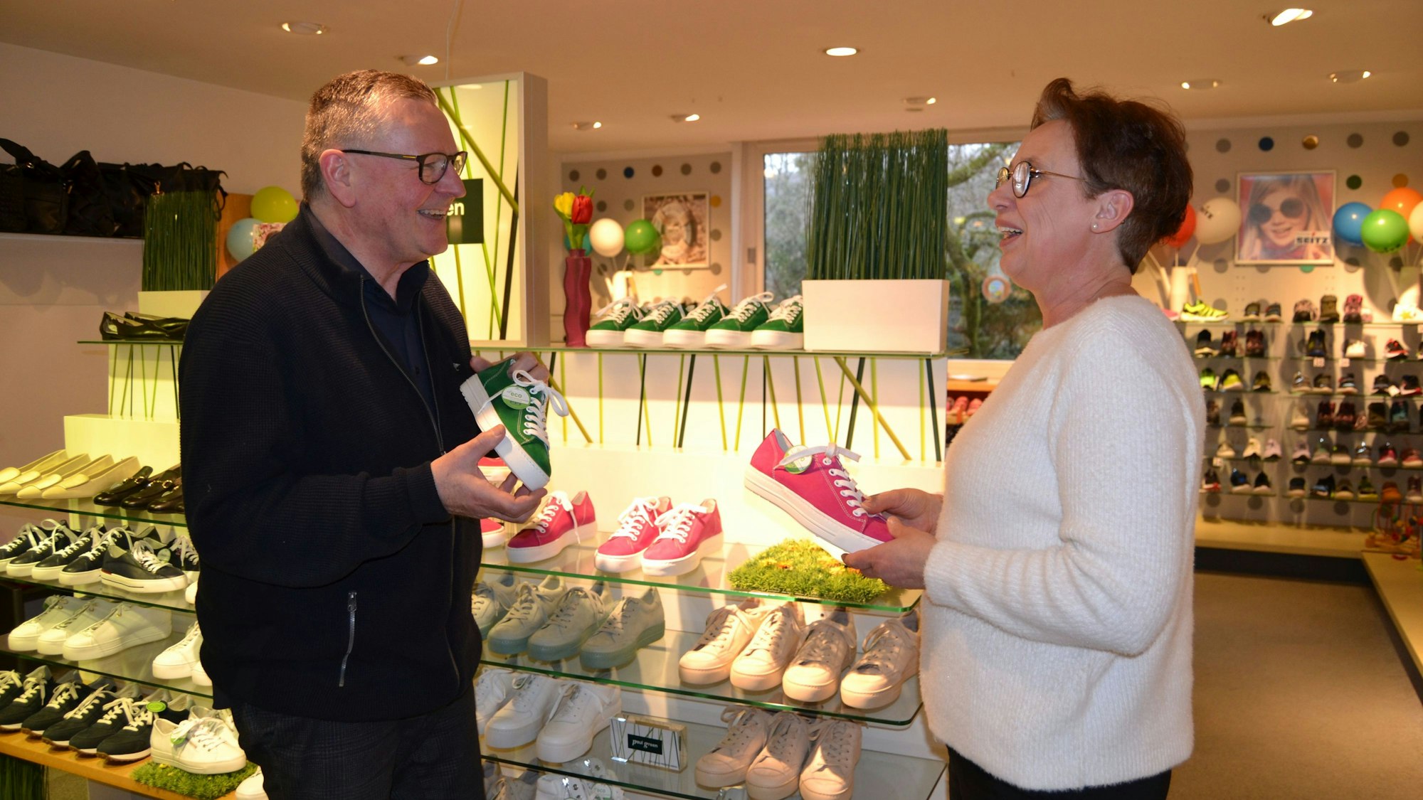 Ein Mann und eine Frau unterhalten sich in einem Schuhgeschäft. Beide halten jeweils einen Schuh in der Hand.