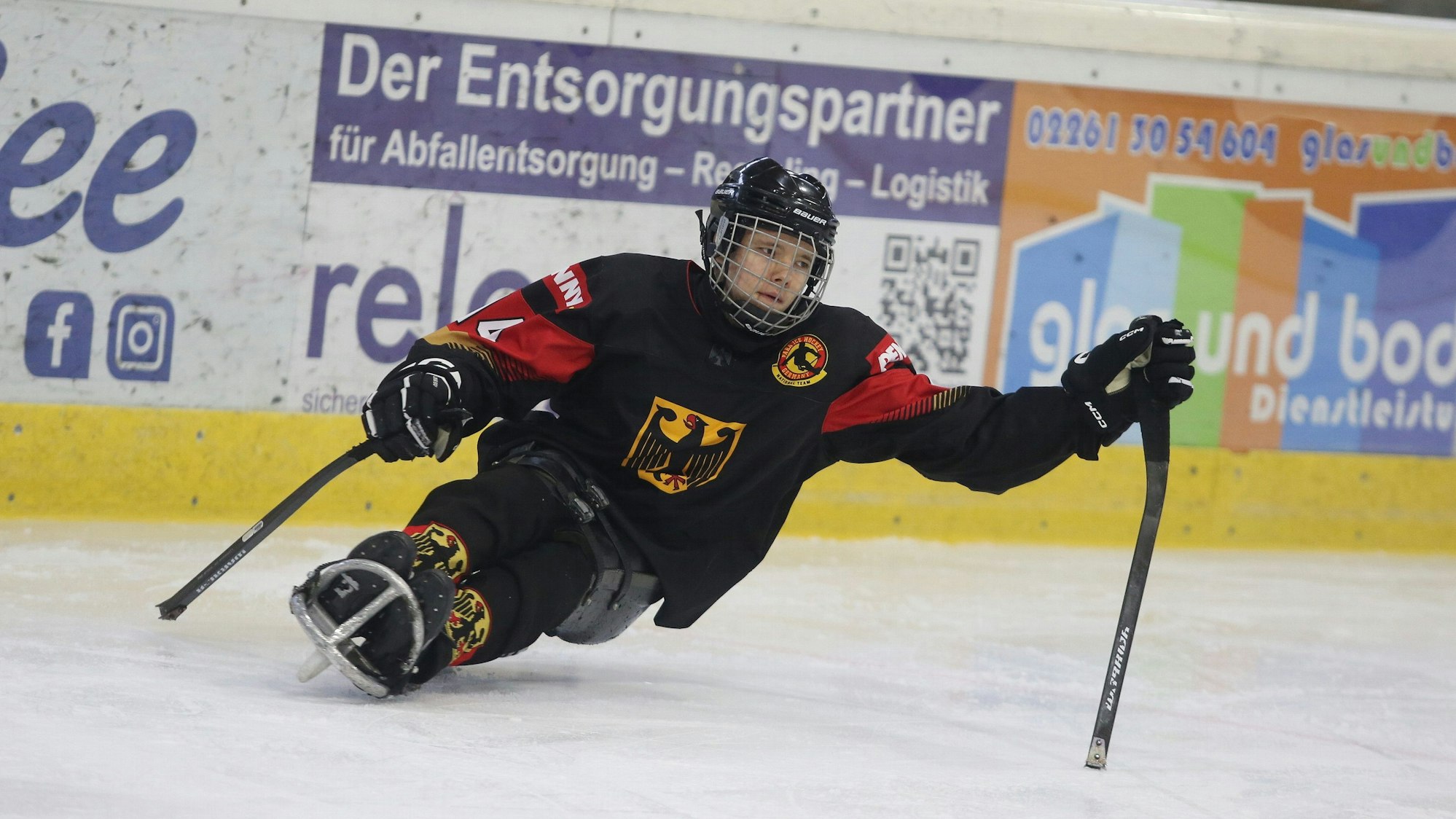 Jano Bußmann sitzt auf dem Schlitten und stößt sich mit den beiden Schlägern ab..