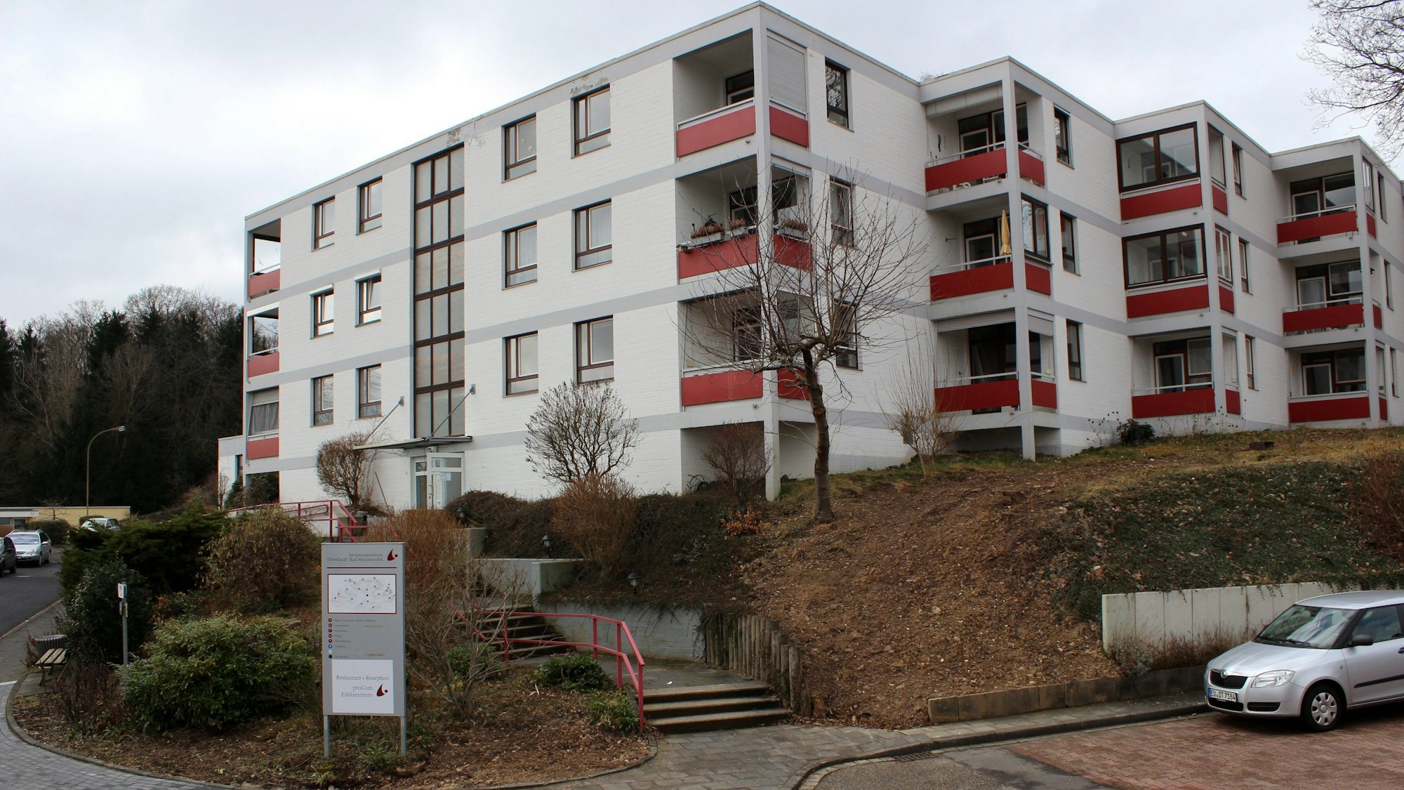 Das Seniorenzentrum Otterbach in Bad Münstereifel steht leicht erhöht. Auf einem Parkplatz rechts unten vor dem Gebäude parkt ein graues Auto. Links unten im Bild führt eine Straße entlang.