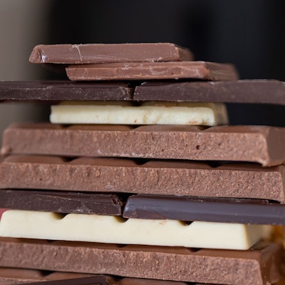Mehrere Stücke von Schokolade liegen aufeinander gestapelt auf einem Tisch. Daneben liegt goldene Verpackung.