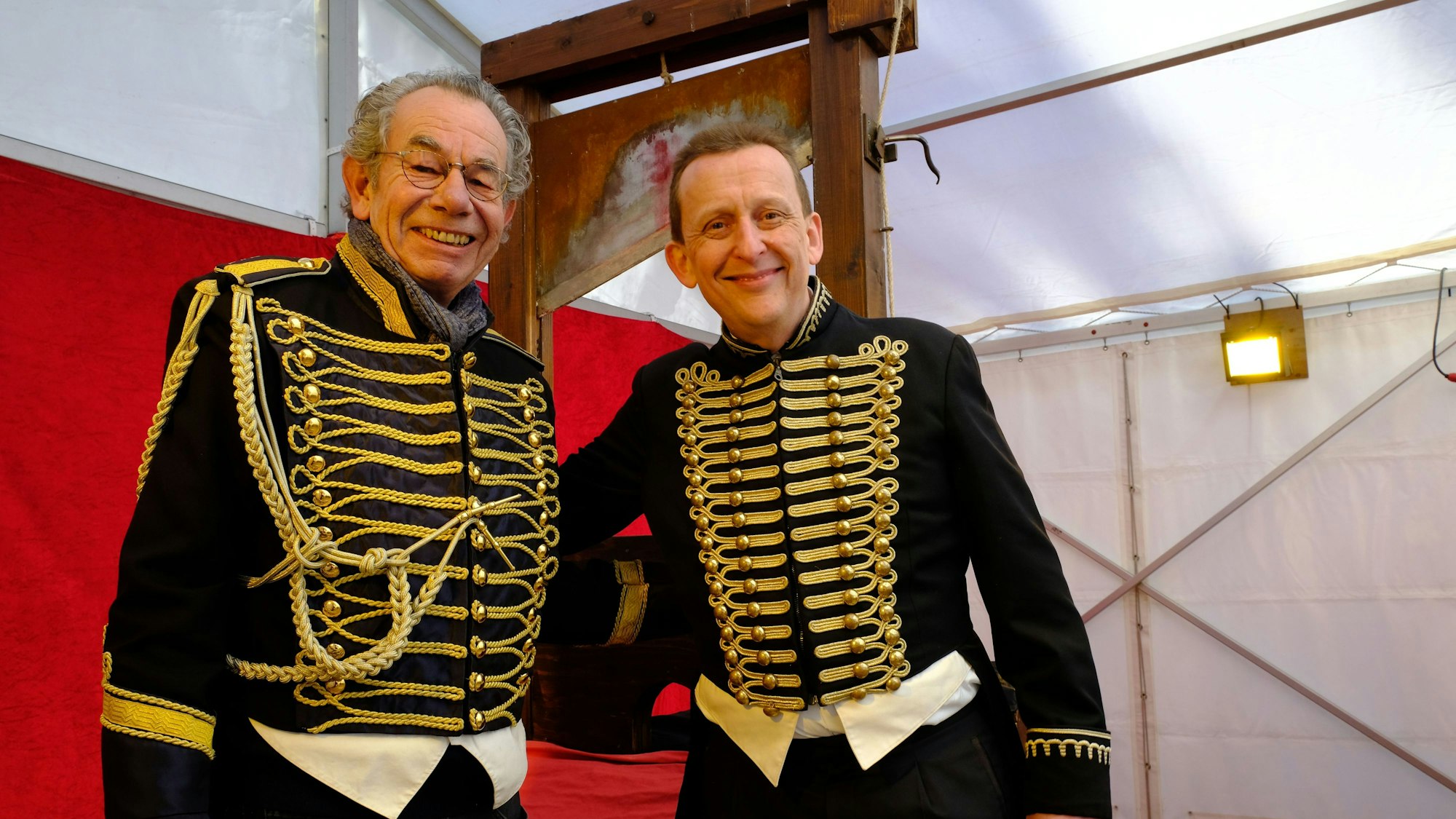 Dr. Michael Faber (l.) übergibt das Fallbeil beim "Jahrmarkt anno dazumal" im Freilichtmuseum Kommern an den Variete-Künstler Jeton.