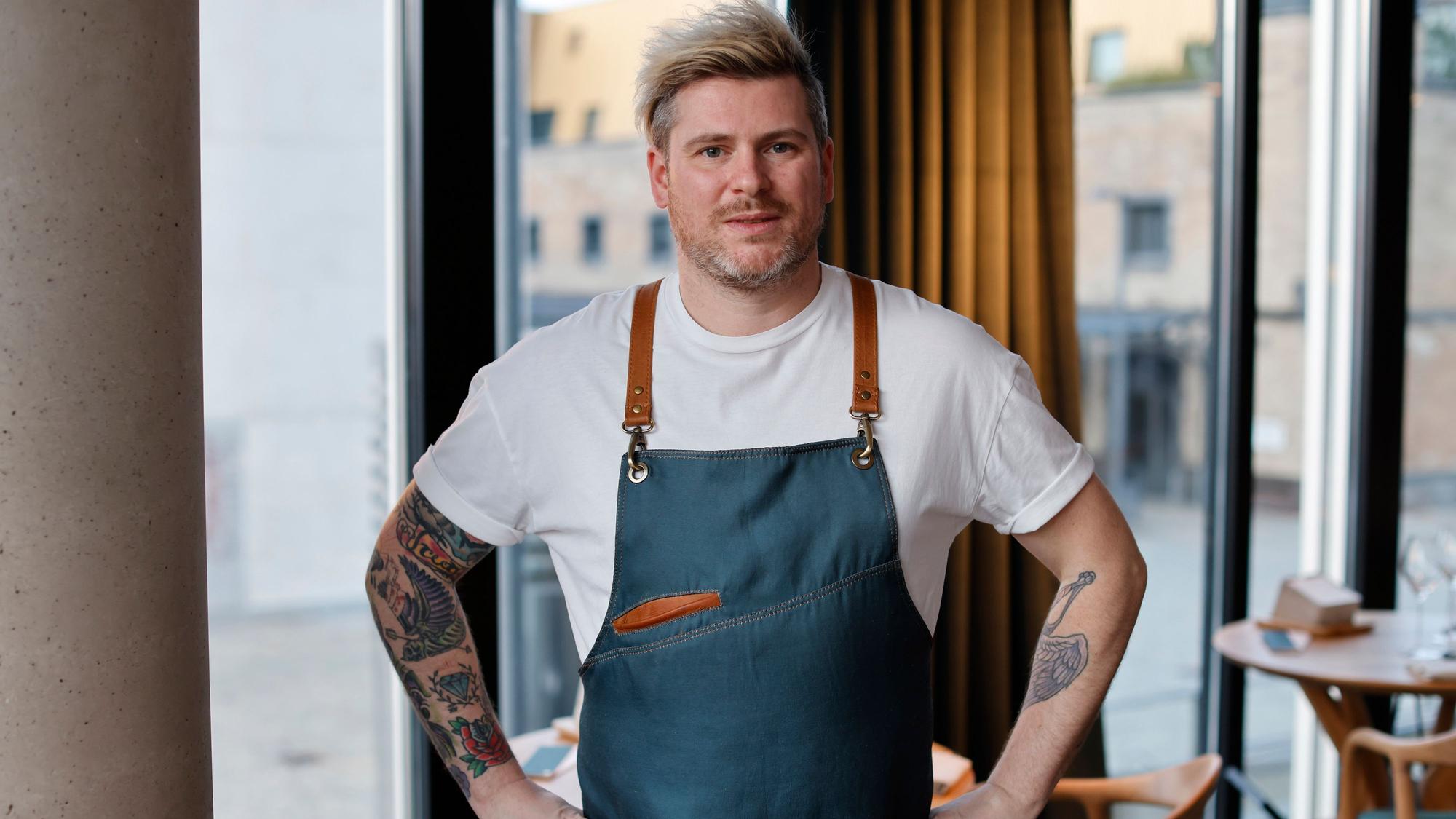 Daniel Gottschlich, Küchenchef und Inhaber des Ox & Klee im Kölner Rheinauhafen psoiert mit einer modern gestalteten Kochschürze für die Kamera.