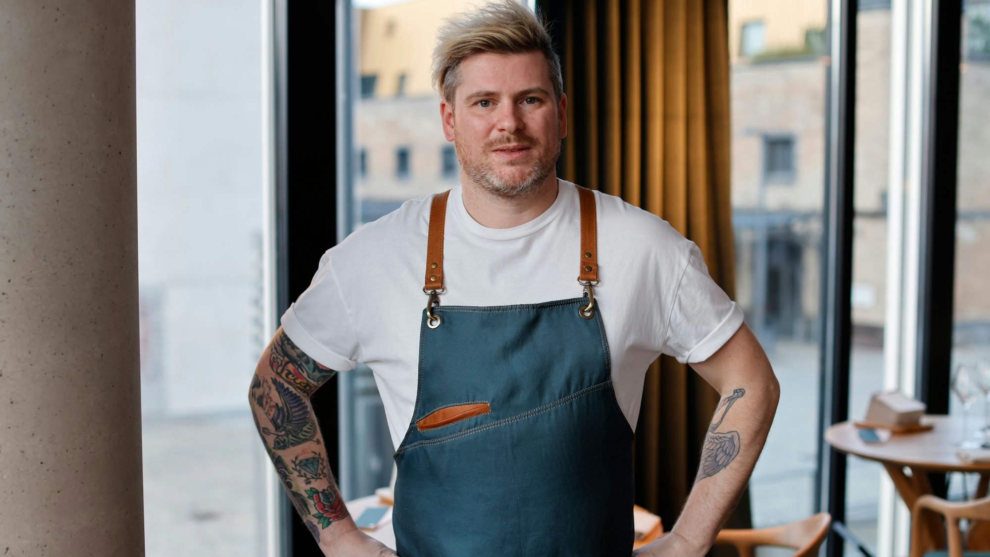 Daniel Gottschlich, Küchenchef und Inhaber des Ox & Klee im Kölner Rheinauhafen psoiert mit einer modern gestalteten Kochschürze für die Kamera.