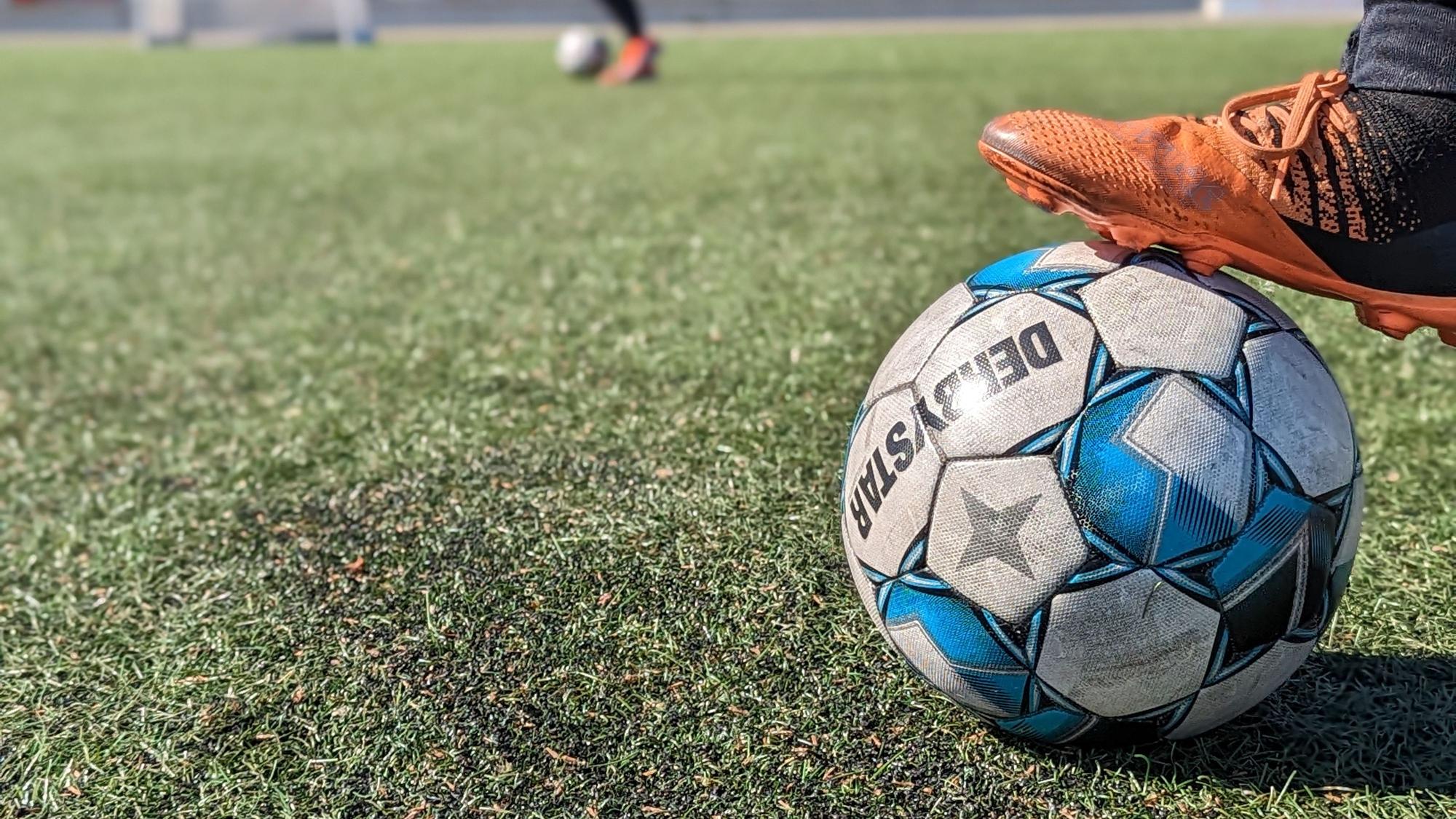 Das Foto zeigt einen Fuß mit Fußballschuh, der auf einem Ball auf einem Kunstrasenplatz steht.