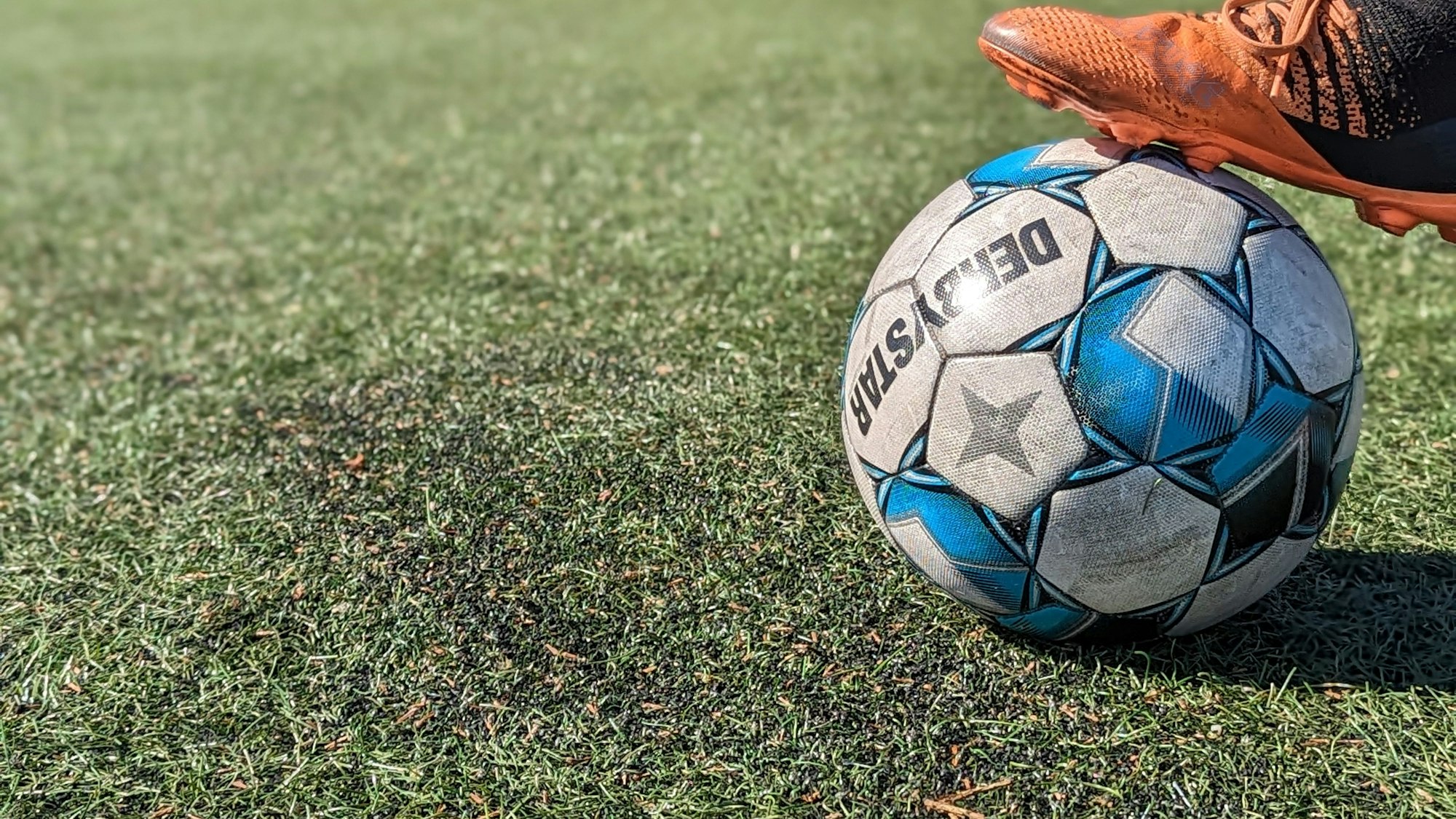 Das Bild zeigt einen Fußball auf dem durch Bengalos beschädigten Kunstrasenplatz.