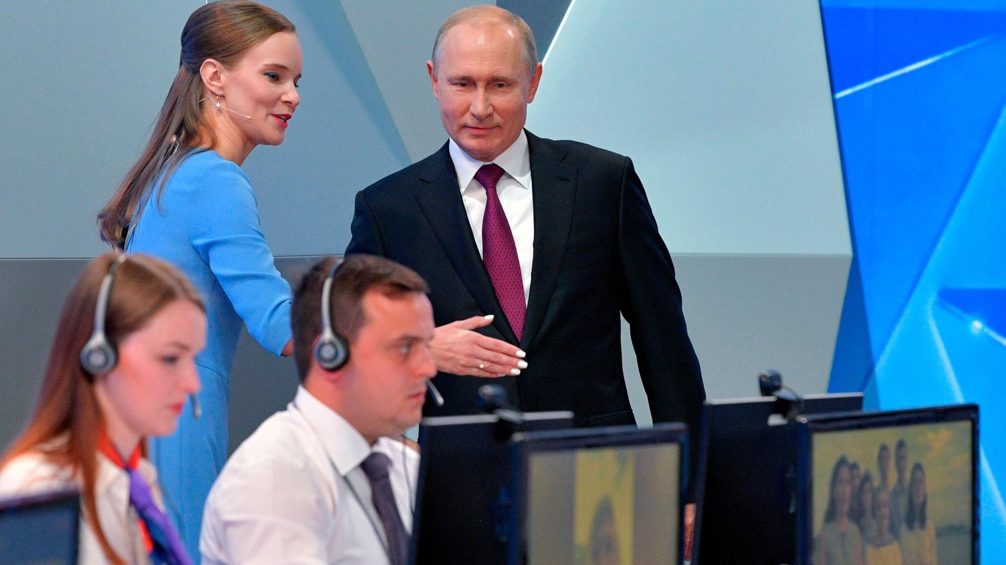 Wladimir Putin (r.), Präsident von Russland, bei einem TV-Auftritt in der Sendung ‚Direkter Draht‘. Eine Mitarbeiterin erläutert dem Kremlchef offenbar die Technik im TV-Studio. Putin selbst soll weder Handy noch Internet benutzen. (Archivbild)