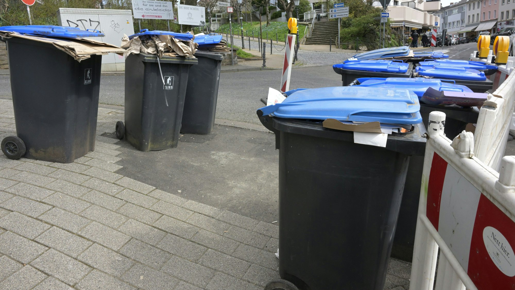 Mehrere Papiermülltonnen stehen ungeleert nebeneinander.