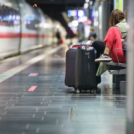 Eine Frau wartet am frühen Morgen mit ihrem Koffer im Frankfurter Hauptbahnhof.