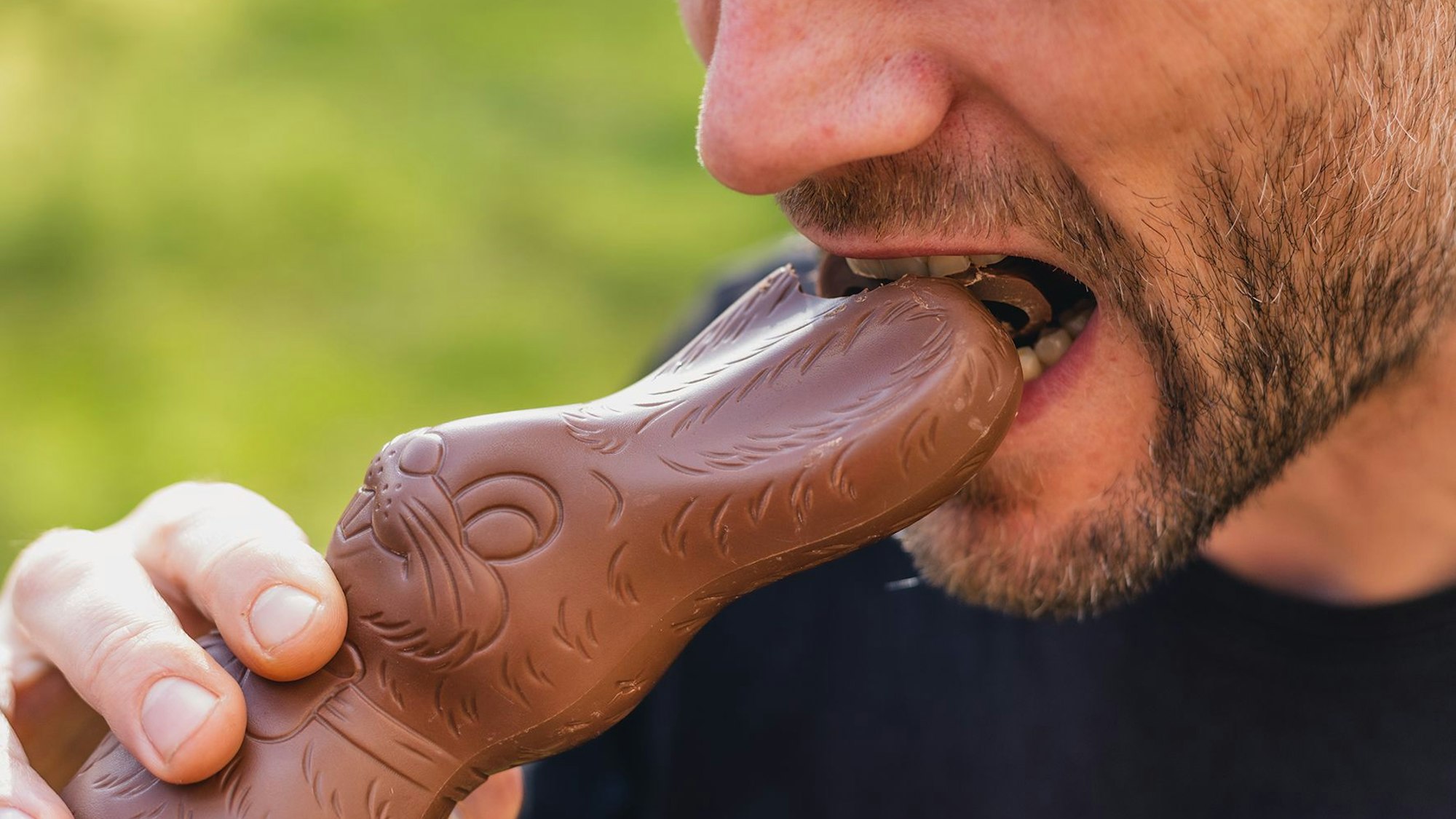 Ein Mann beißt in einen Schokohasen.