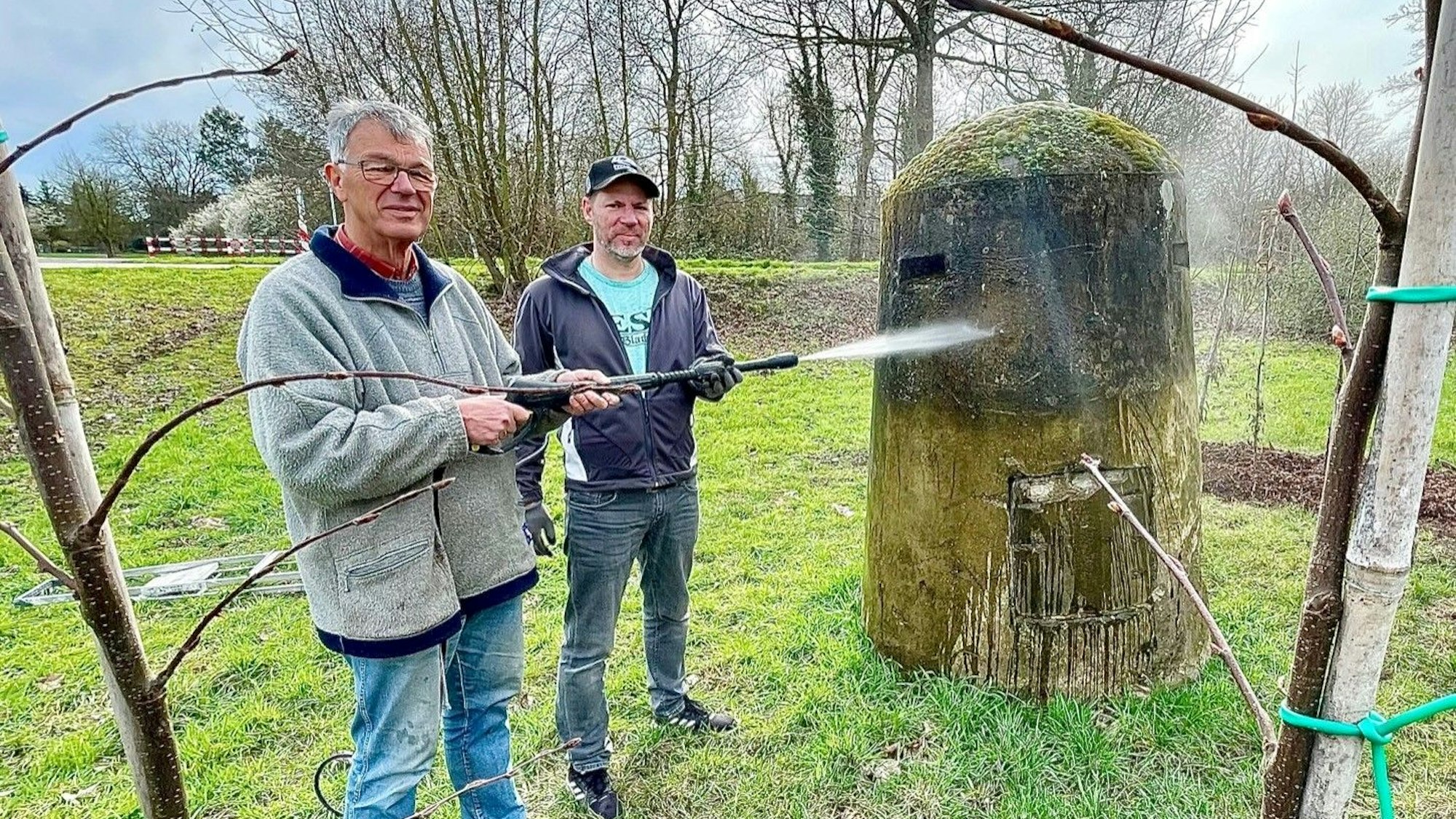 Die beiden Männer stehen seitlich vor dem Bunker und säubern ihn mit einem Hochdruckreiniger.