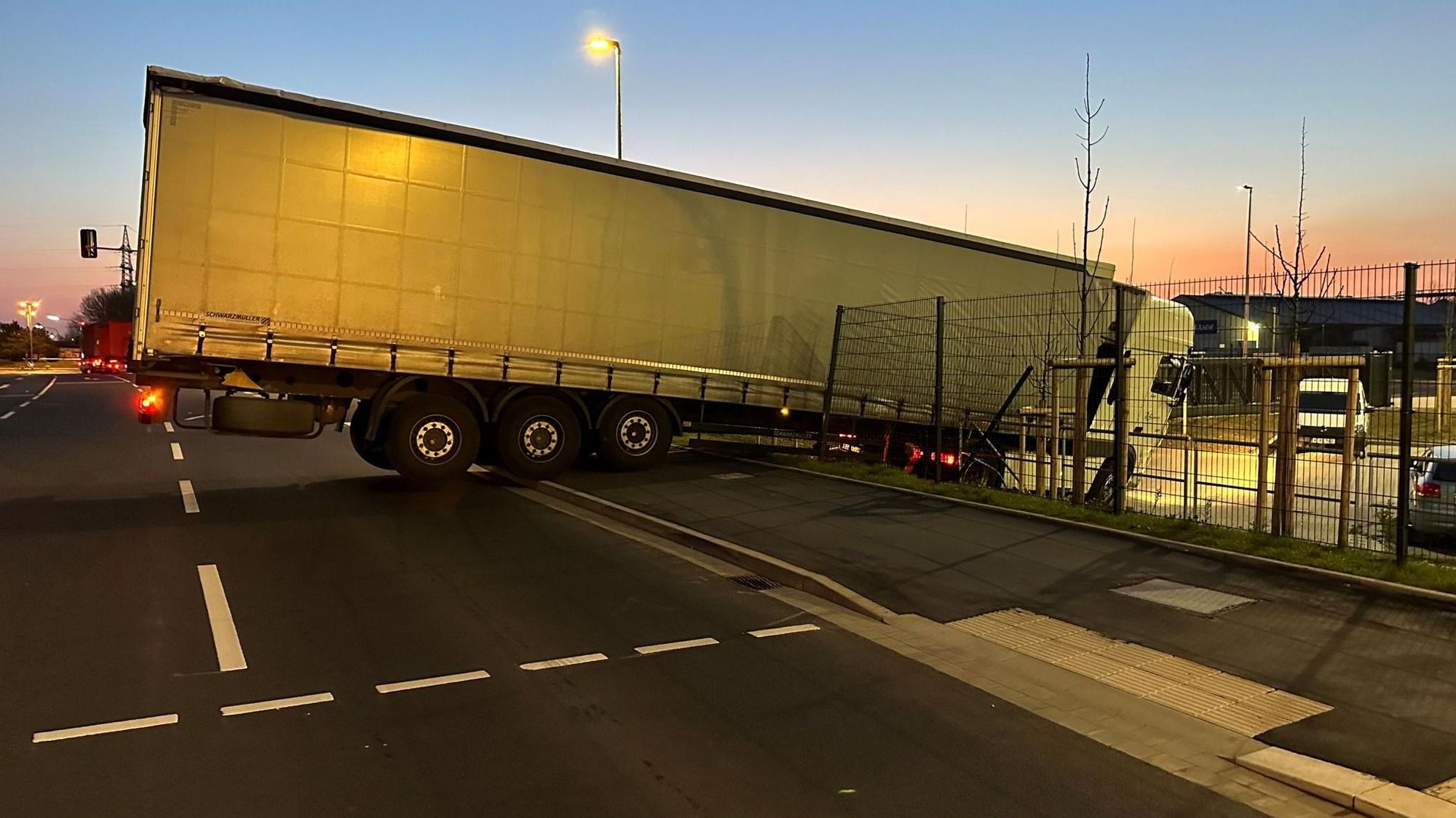 Ein Lkw steht halb auf der Straße, der vordere Teil samt Zugmaschine hat einen Zaun durchbrochen und ist auf einen tiefer gelegenen Parkplatz gestürzt