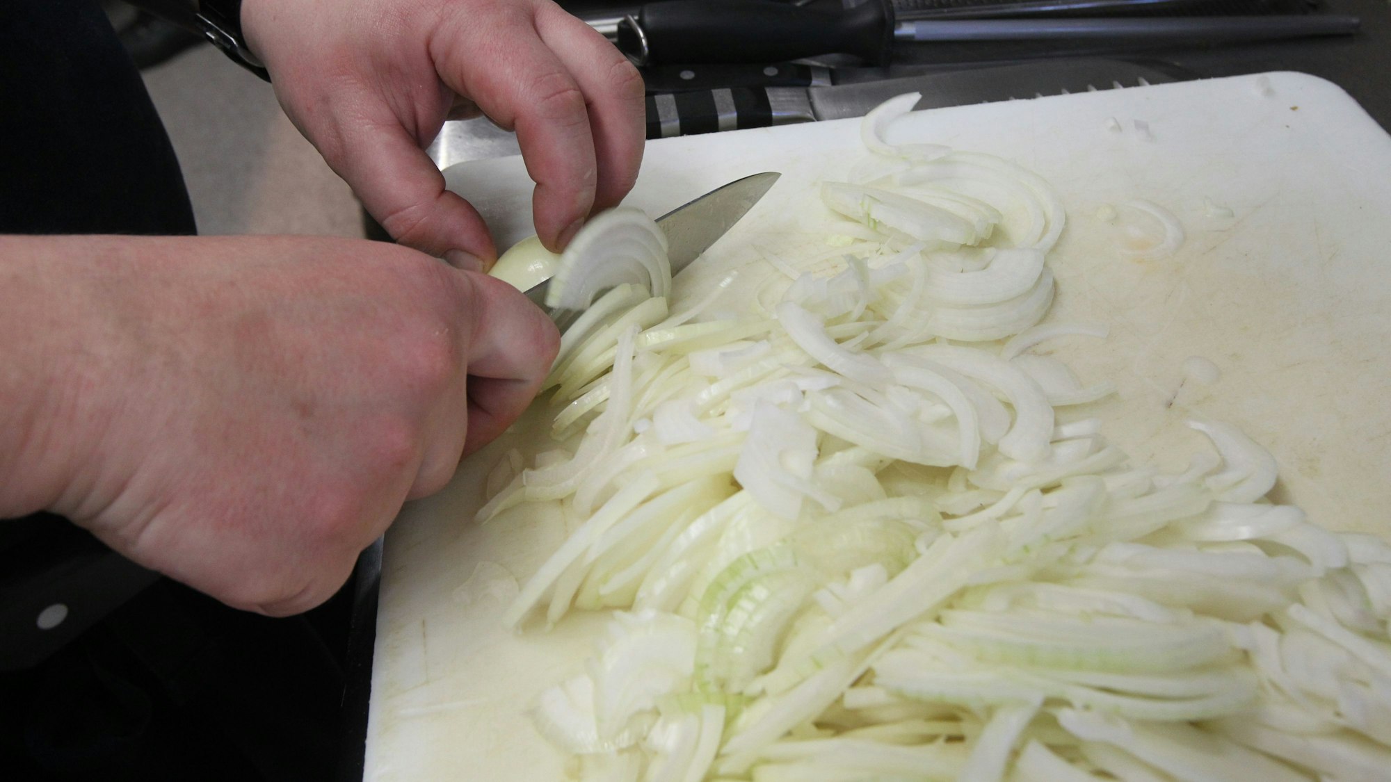 Zwei Hände schneiden mit einem scharfen Messer eine Zwiebel.