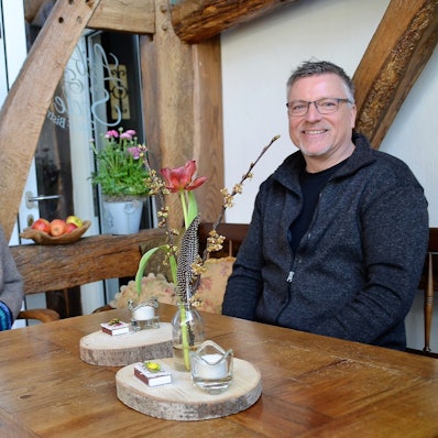 Eine Frau und ein Mann sitzen an einem Holztisch eines Cafés. Im Hintergrund sind Holzbalken zu sehen.