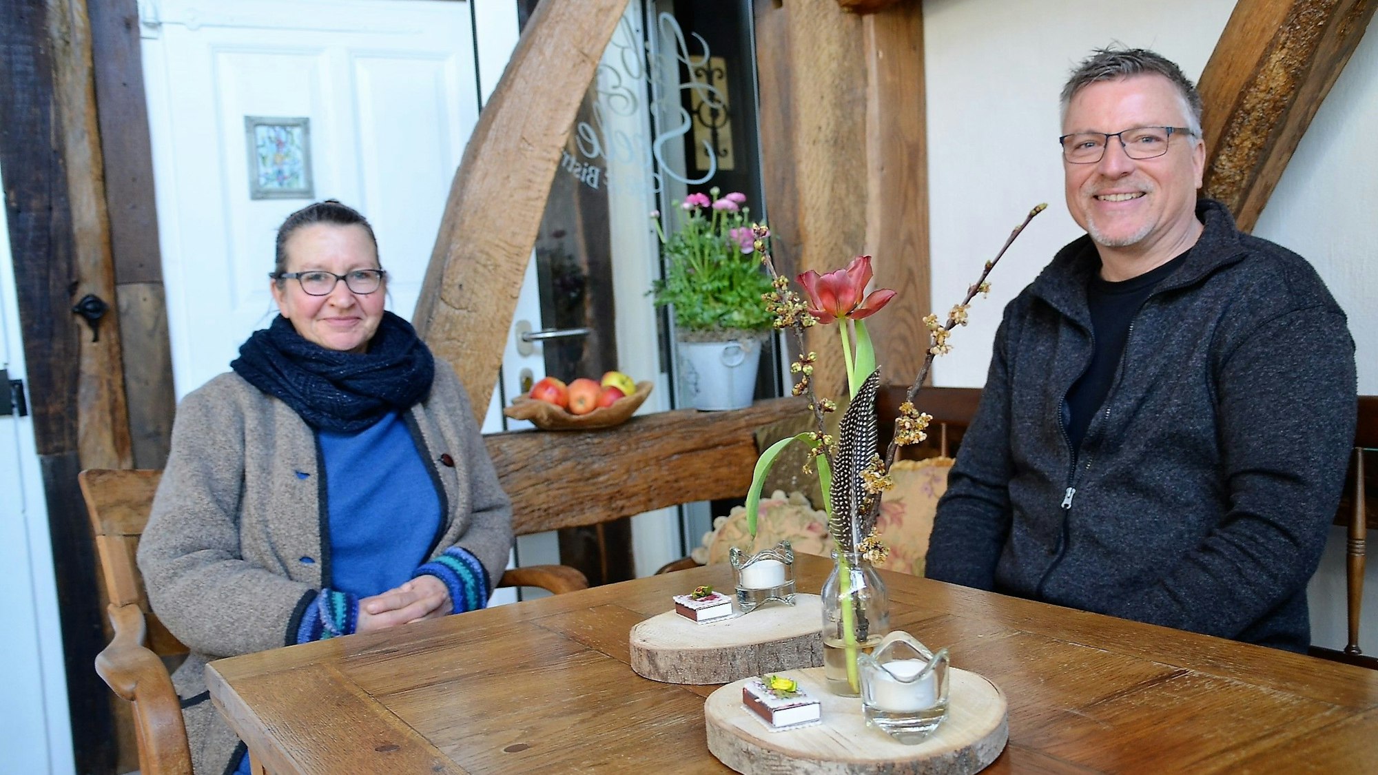 Eine Frau und ein Mann sitzen an einem Holztisch eines Cafés. Im Hintergrund sind Holzbalken zu sehen.