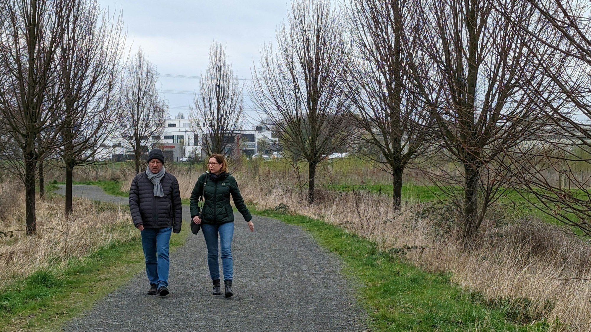Zwei Spaziergänger sind auf dem Schotterweg unterwegs.