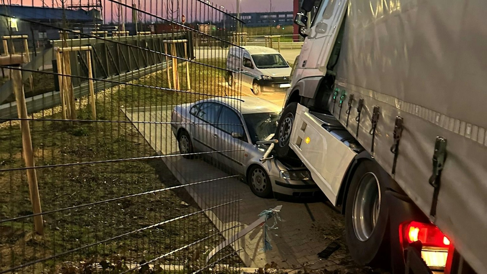 Ein Lastwagen steht mit der Zugmaschine auf einem demolierten Auto. Im Vordergrund ist ein durchbrochener Zaun zu sehen.