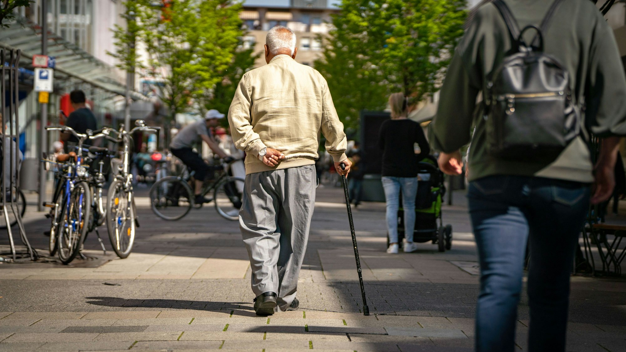 Ein älterer Herr mit Stock geht in einer Fußgängerzone entlang.