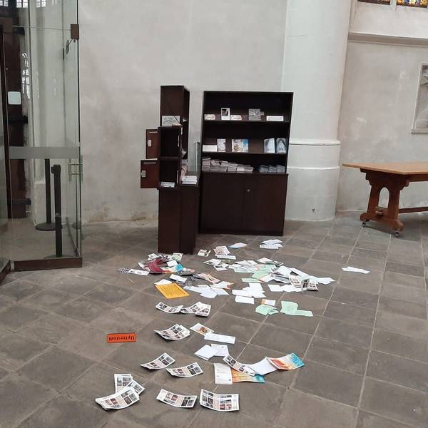 Broschüren und Schriften liegen auf dem Boden neben einer Kirchentür, der Schriftenstand ist aufgebrochen, Opferstöcke sind komplett gestohlen worden. Auf dem Boden liegt ein Schild mit der Aufschrift „Opferstock“.