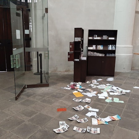 Broschüren und Schriften liegen auf dem Boden neben einer Kirchentür, der Schriftenstand ist aufgebrochen, Opferstöcke sind komplett gestohlen worden. Auf dem Boden liegt ein Schild mit der Aufschrift „Opferstock“.