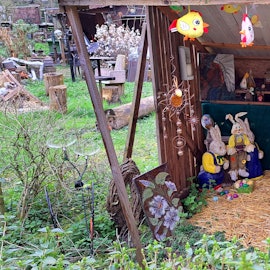 Hasenfiguren stehen in einem Unterstand, auf einem großen bunten Osterei steht „Frohe Ostern“.