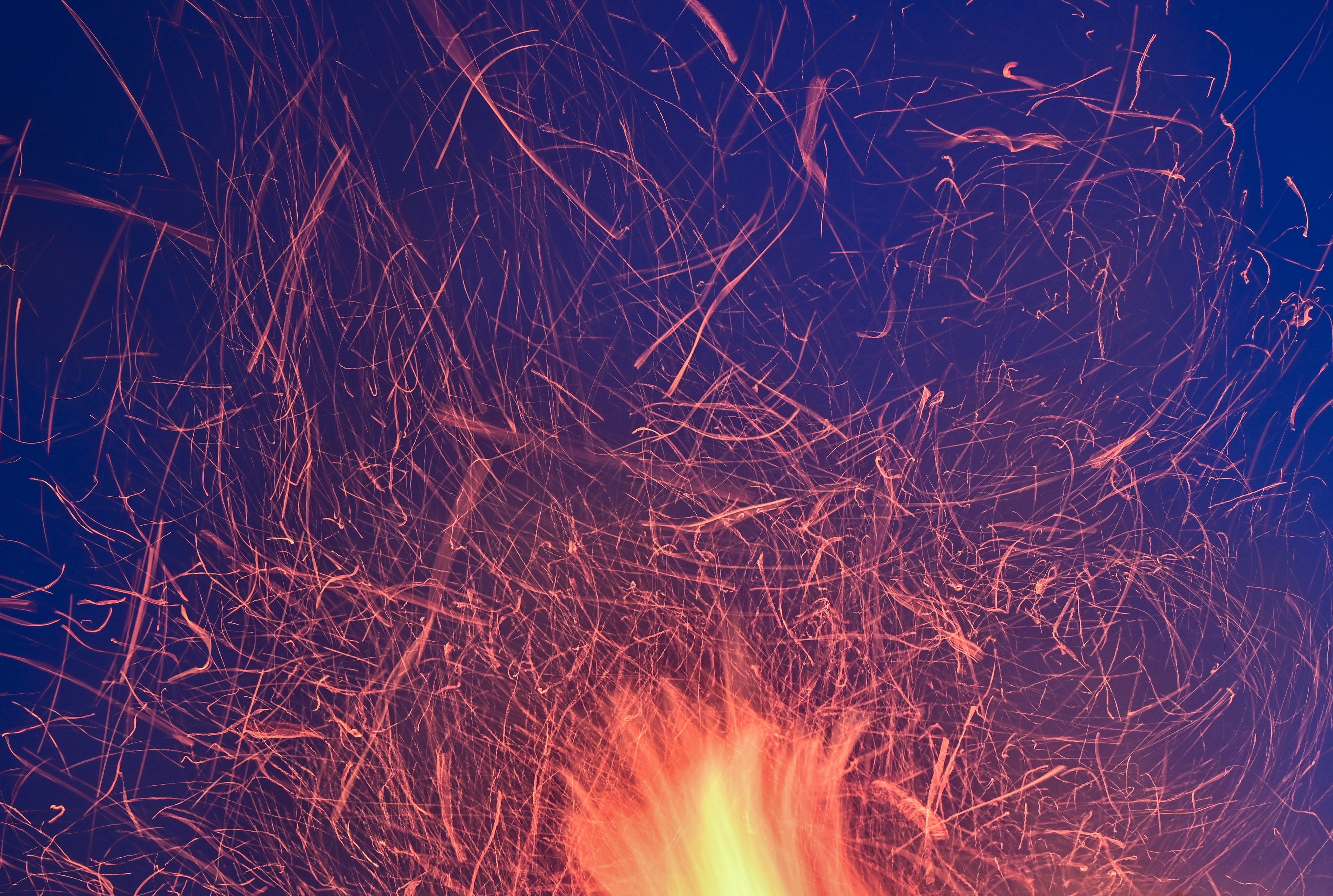 Funken eines Osterfeuers heben sich als Lichtspuren vor dem blauen Abendhimmel ab.