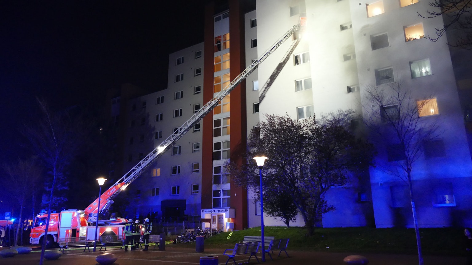 Feuerwehrfahrzeug mit Kran vor einem brennenden Hochhaus