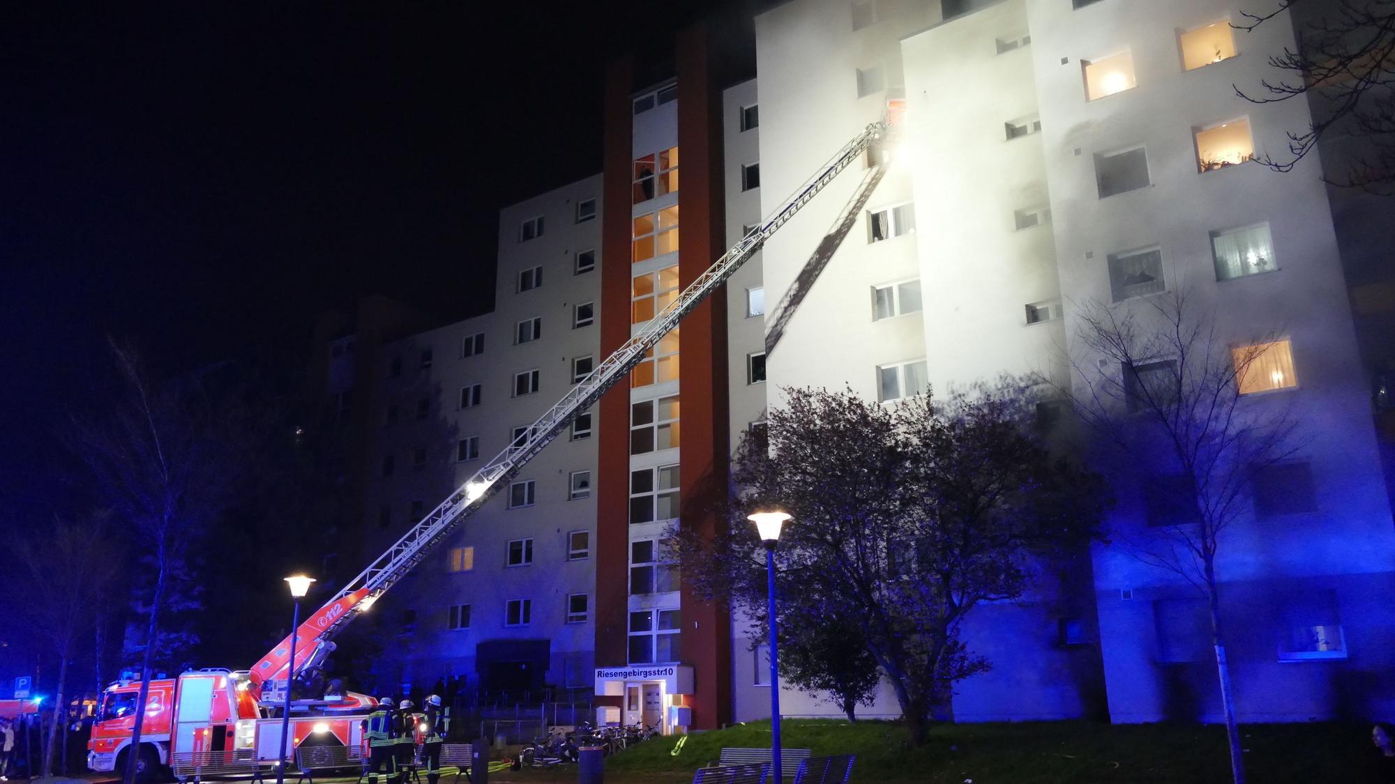 Feuerwehrfahrzeug mit Kran vor einem brennenden Hochhaus