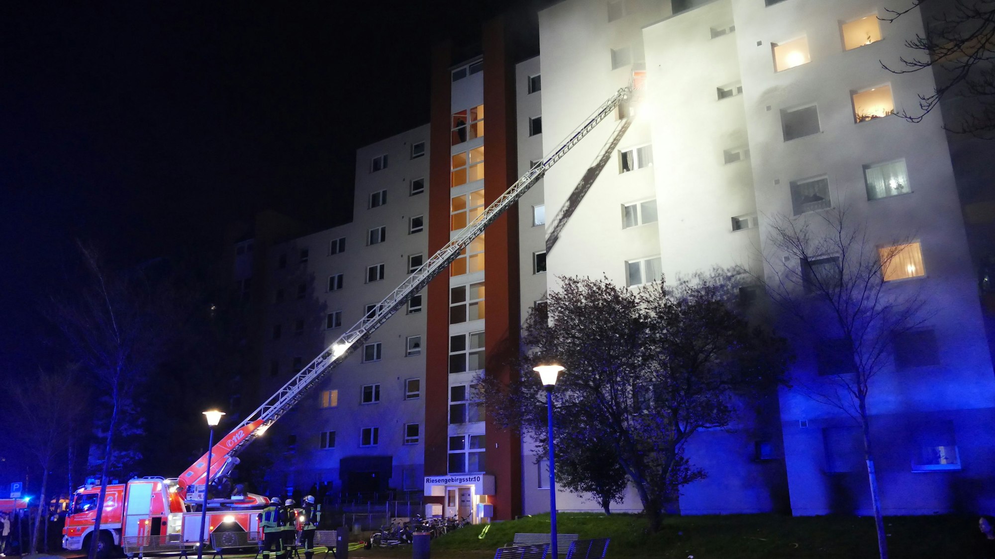 Feuerwehrfahrzeug mit Kran vor einem brennenden Hochhaus